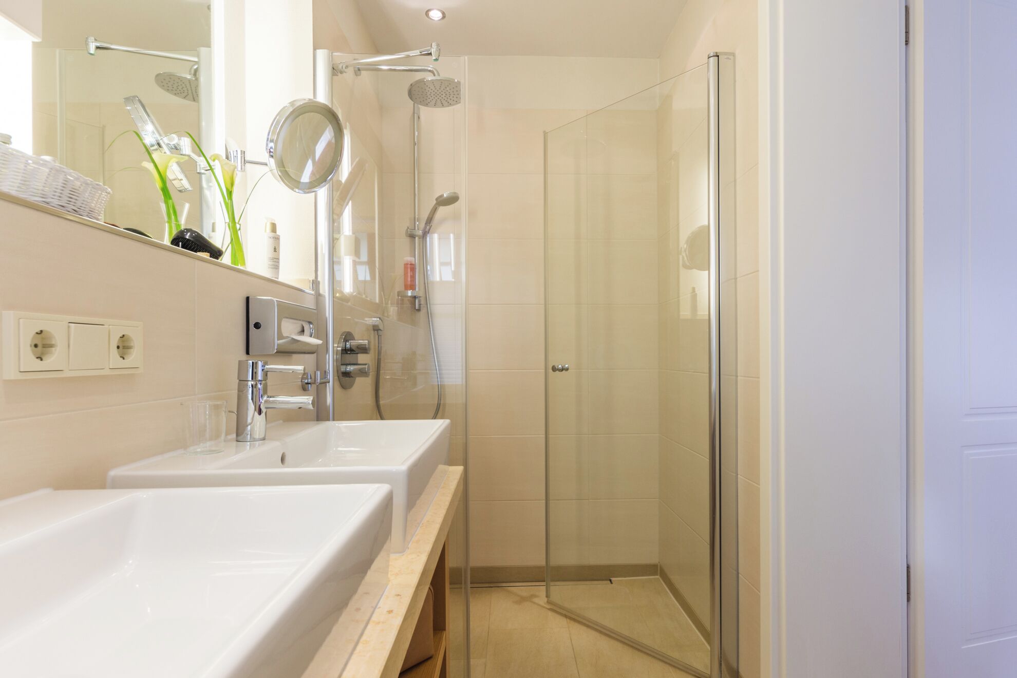 A modern bathroom with two sinks, a glass shower enclosure, and a mirror.