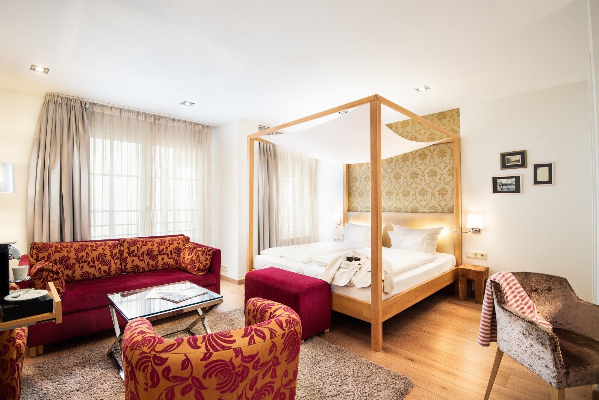 A hotel room with a four-poster bed, a red sofa, a small table, and a wooden bench.