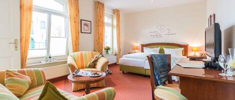 A hotel room with a bed, a sofa, a chair, a desk, and a television.