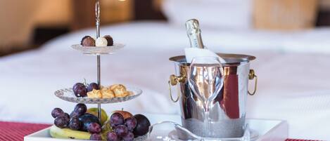 A three-tiered dessert stand with assorted sweets and a fruit platter, a champagne bucket, and a bottle of champagne on a white tray.