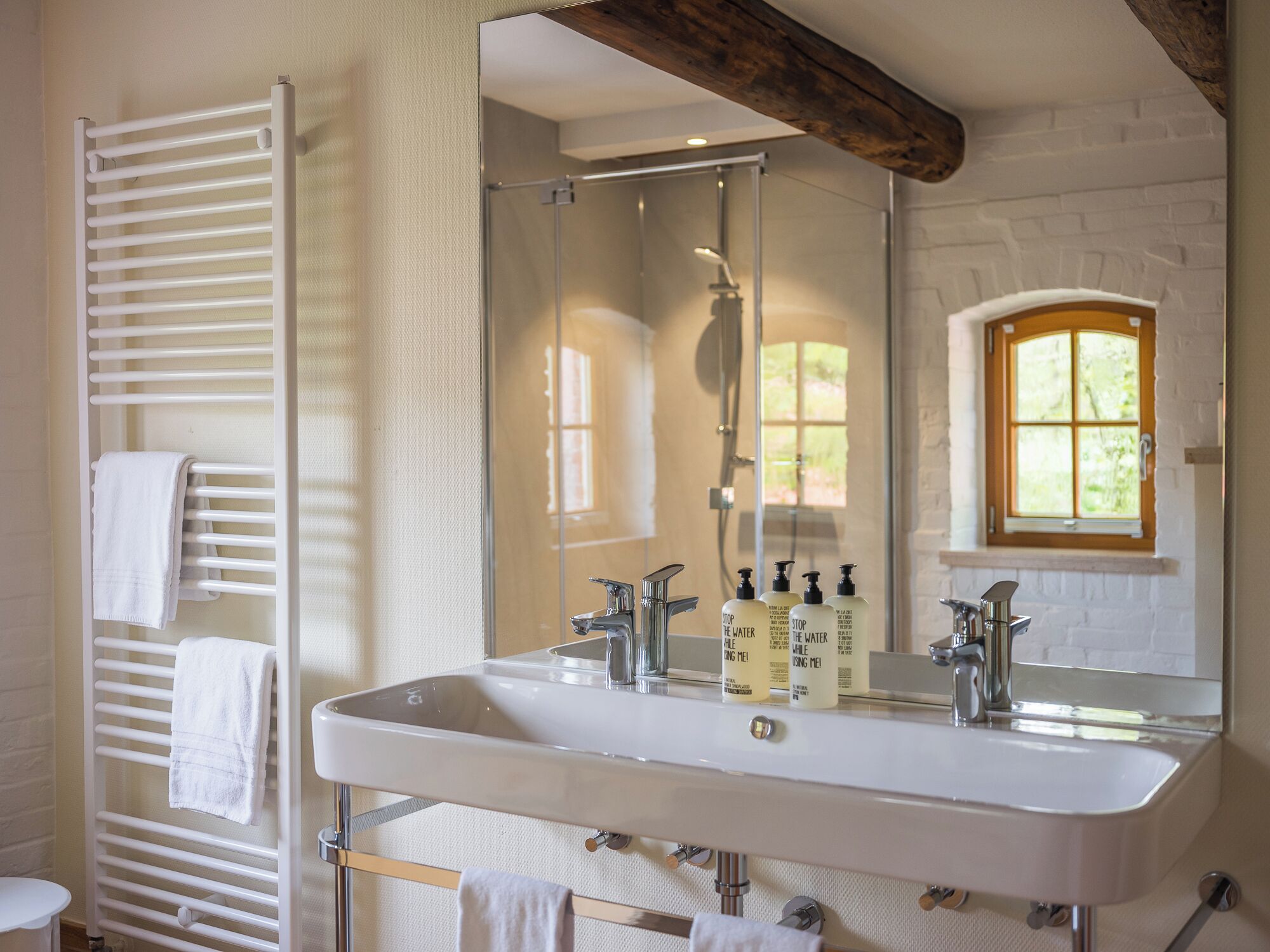 A bathroom with a large mirror, a shower, a sink with two faucets, and a towel rack.