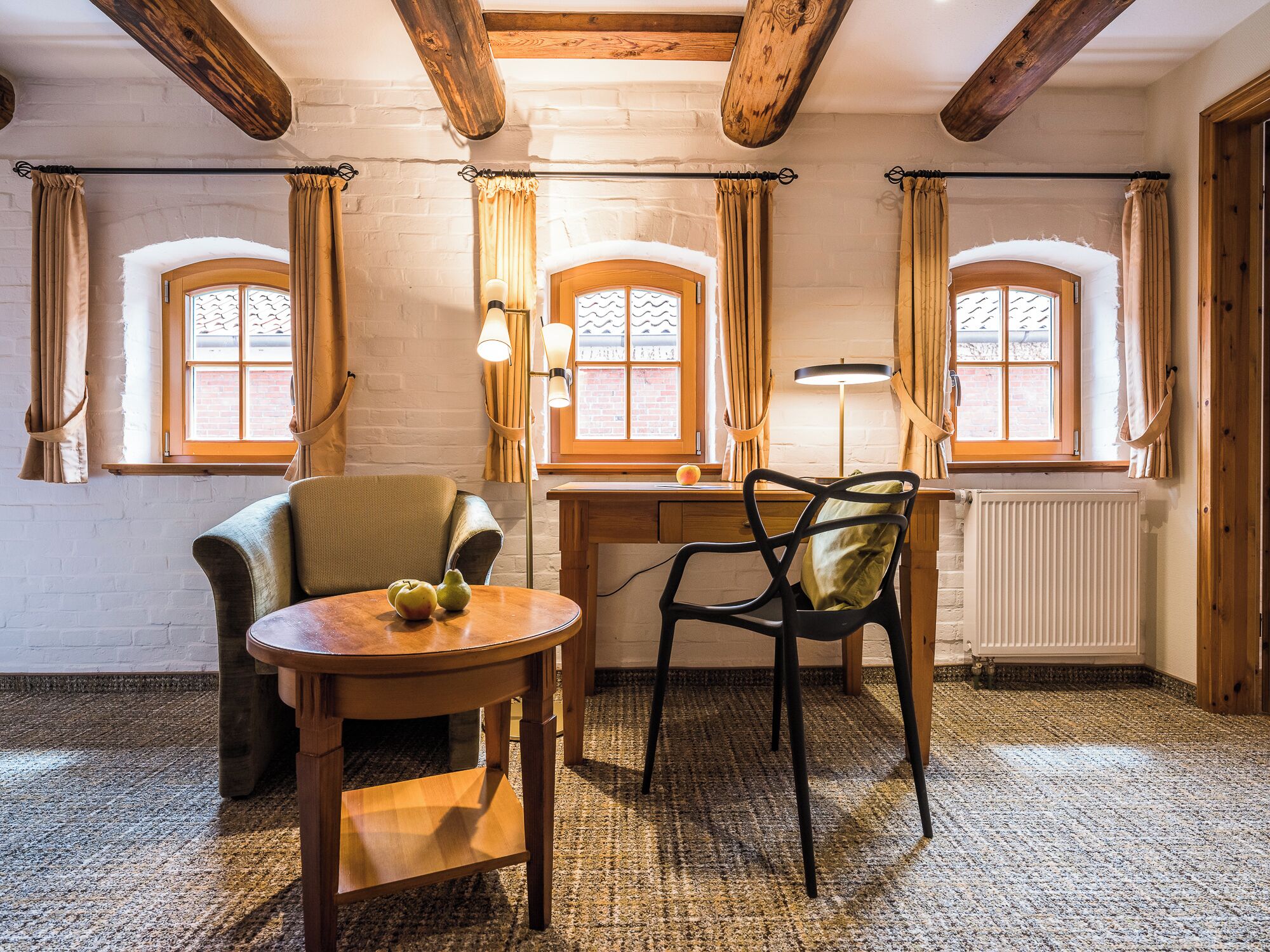 A cozy room with a wooden table and chairs, a radiator, and windows with curtains.