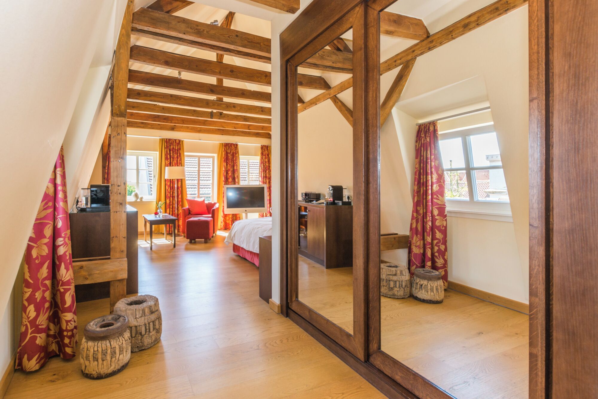 Ein Zimmer mit Holzboden, einem Bett, einem Fernseher, einem Schreibtisch und einem Vorhangfenster.