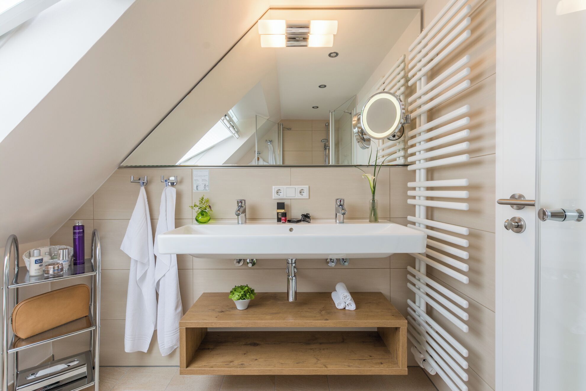 A modern bathroom with a skylight, a large mirror, a wooden vanity, and a towel rack.