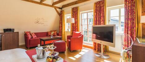 A cozy hotel room with a wooden ceiling, a sofa, a TV, and a dining area with a fruit display.