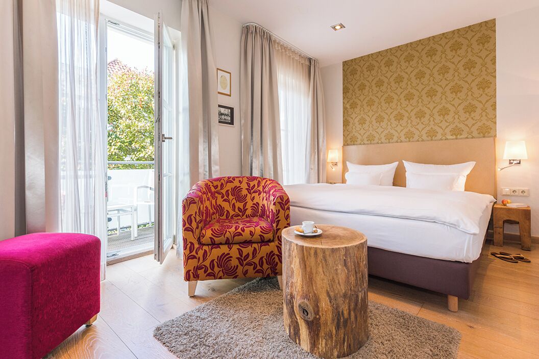 Quarto de hotel com cama, uma cadeira, uma mesinha e vista para o exterior.