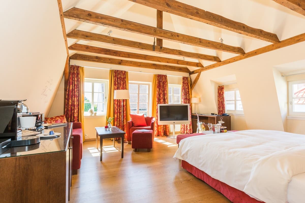 Une chambre d’hôtel avec un plafond en bois, un lit, un bureau avec un ordinateur, une télévision et une fenêtre avec des rideaux.