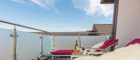 Ein Balkon mit roten, gepolsterten Loungesesseln, einem kleinen Tisch mit Flasche und Gläsern sowie Meerblick.