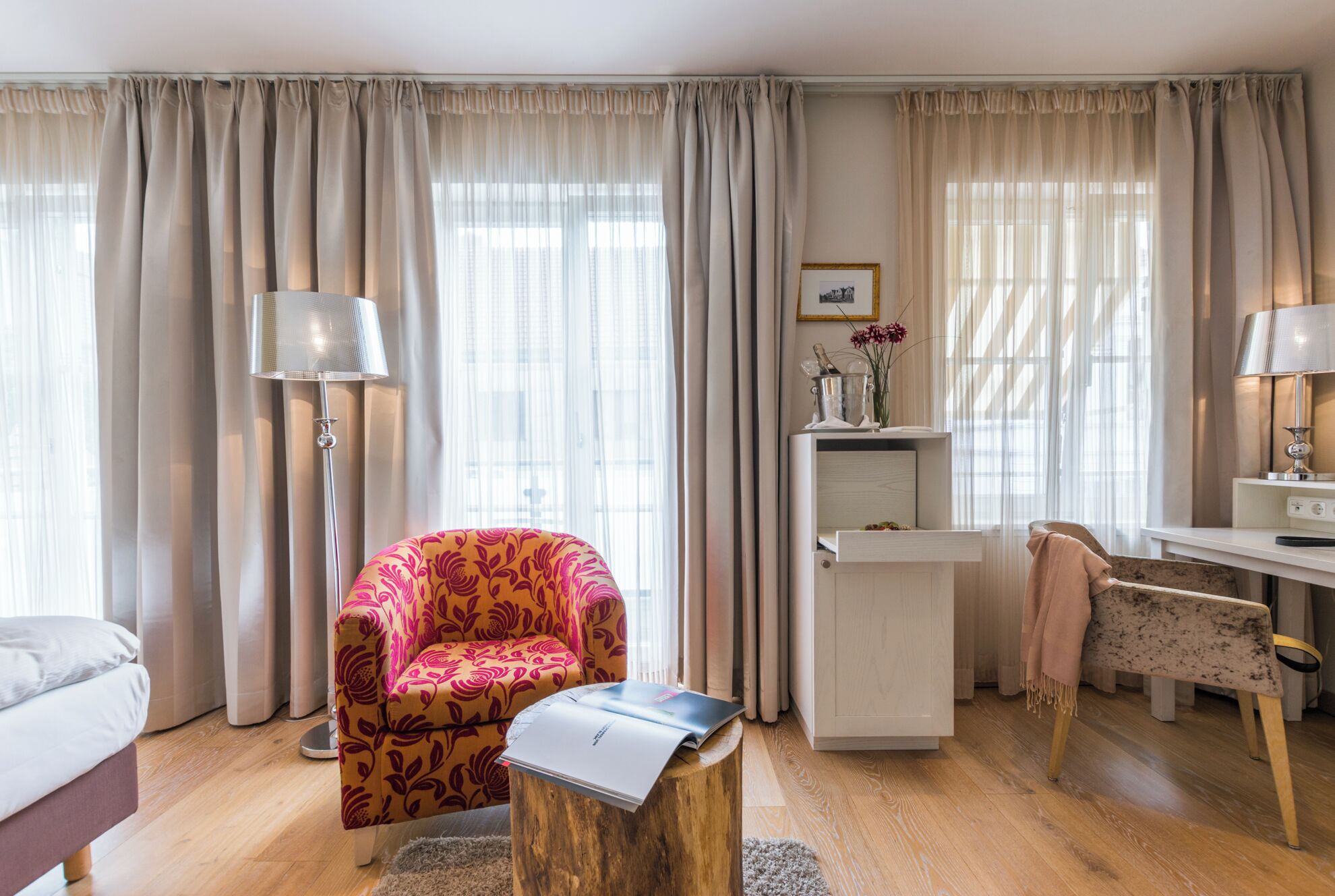 Una habitación bien iluminada con suelo de madera, un escritorio con lámpara, una silla y una cama.