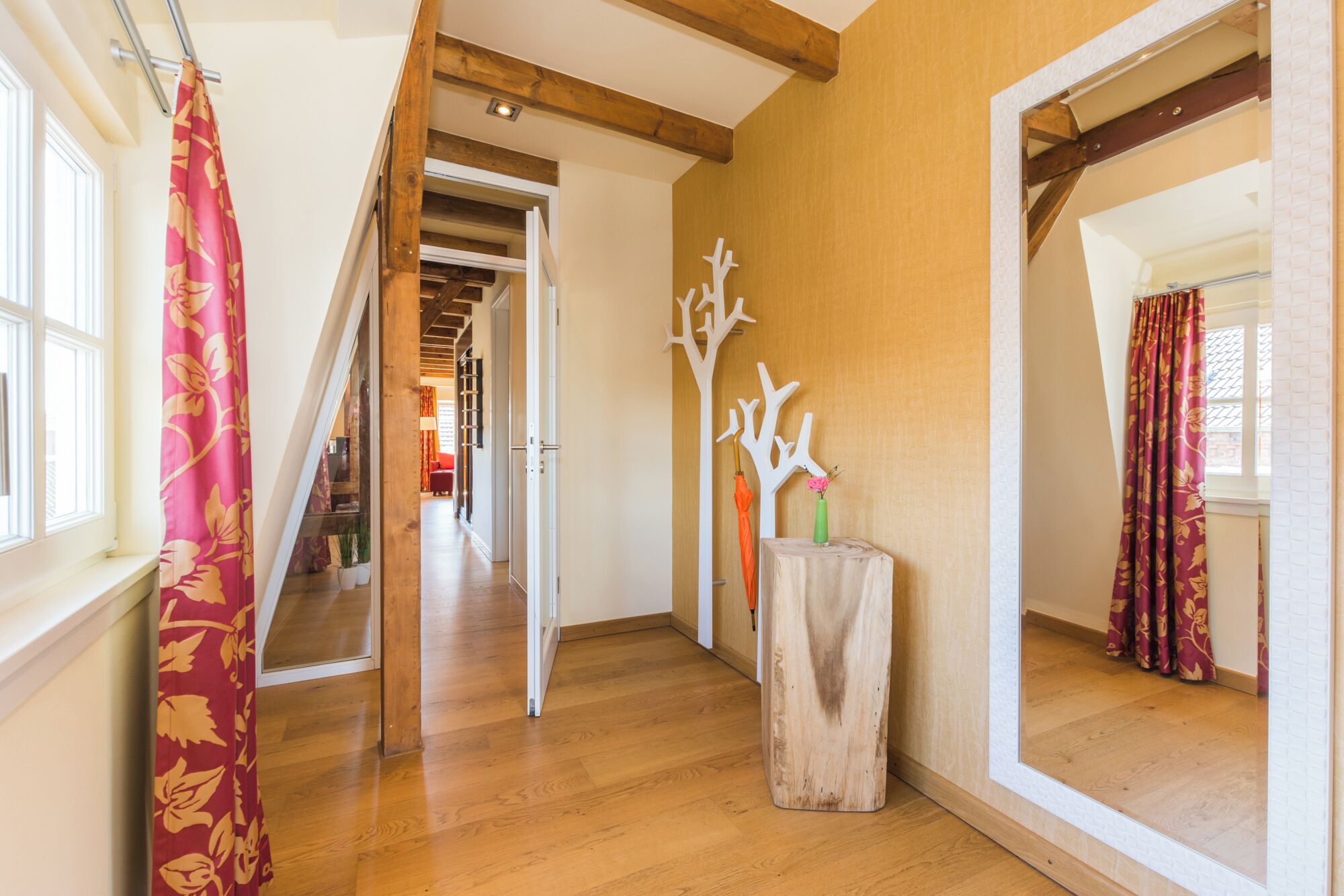 A hallway with wooden flooring, a mirror, and a wooden tree sculpture.