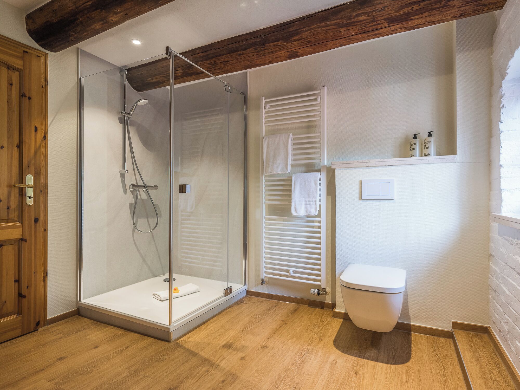 A modern bathroom with a glass-enclosed shower, a white toilet, and wooden flooring.
