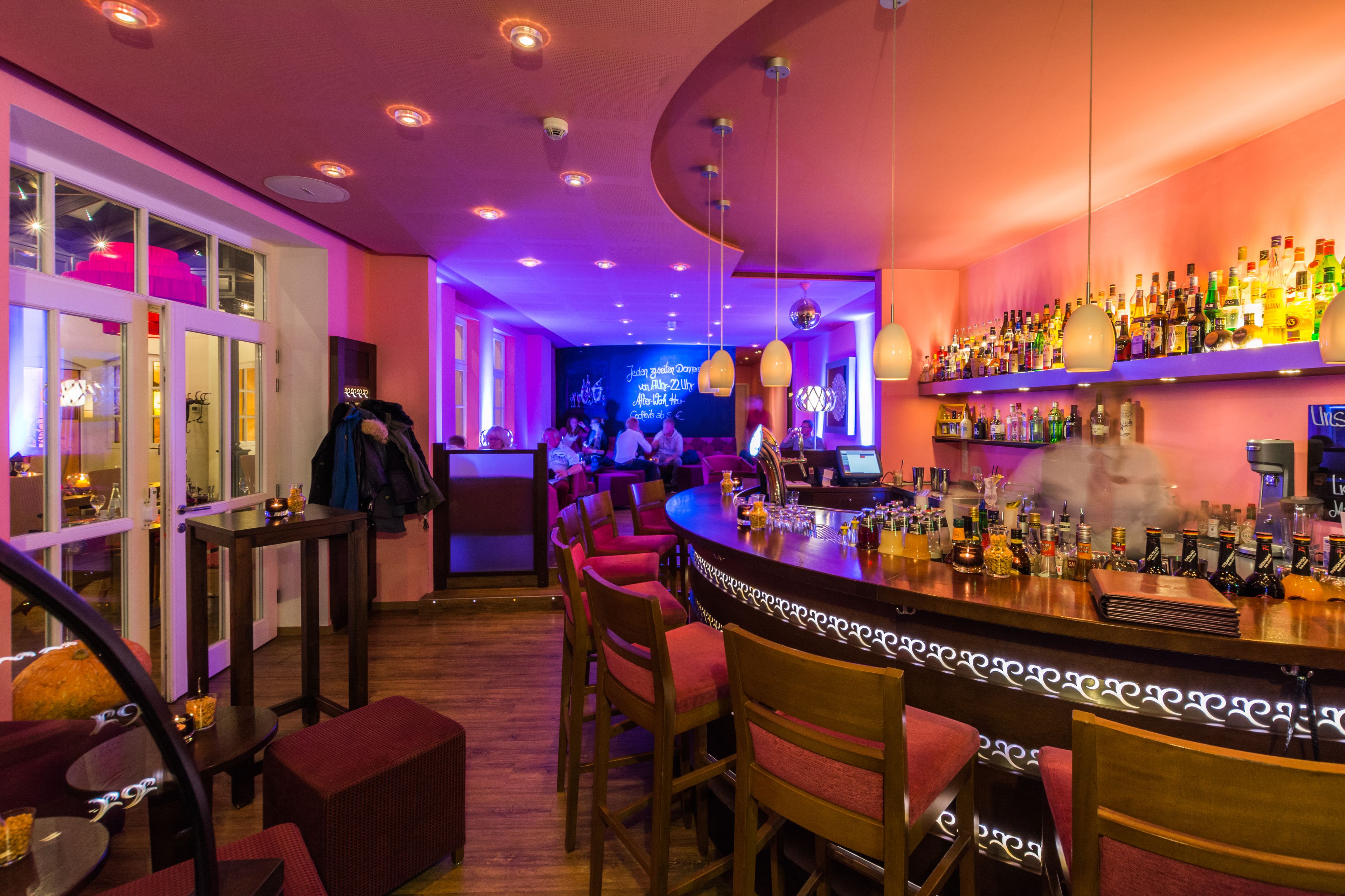 A bar area with a curved counter, multiple seating options, and a variety of bottles on shelves.