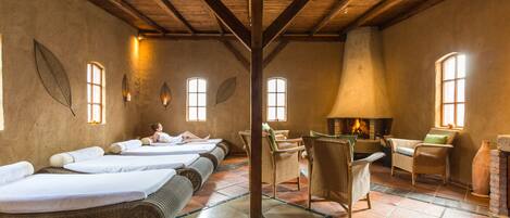 Una habitación con cuatro camas, muebles de mimbre, chimenea y suelo de baldosas.