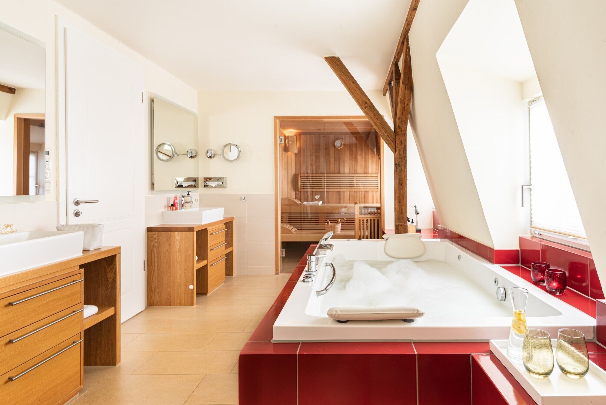 A modern bathroom with a large bathtub, wooden vanity, and a sauna visible through a glass door.