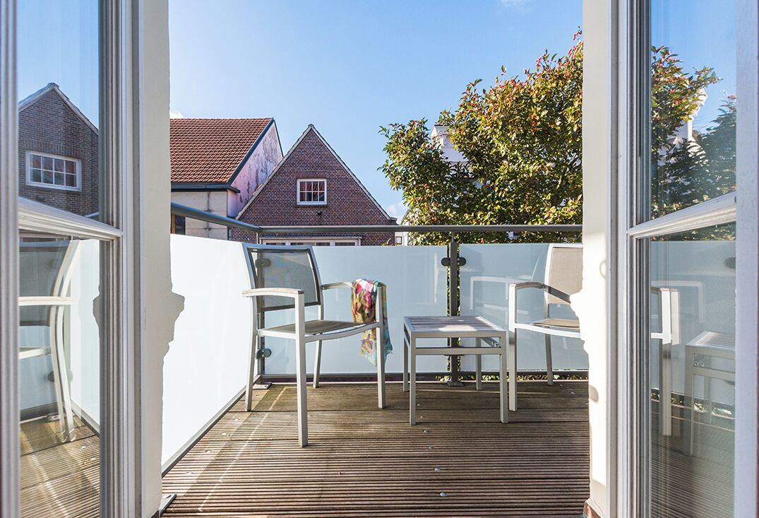 Un balcón con dos sillas blancas y una mesa, con vista a una casa de ladrillo y un árbol.