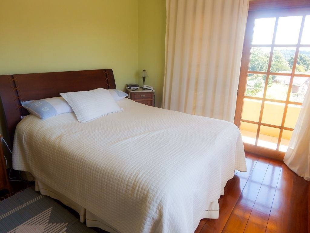 A neatly made bed with a wooden headboard, a bedside table with a lamp, and a view of greenery through a window.