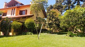Una casa con techo inclinado, un balcón y un jardín con diversas plantas y árboles.