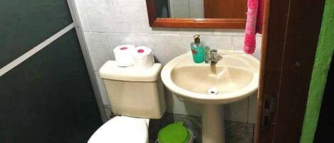 A small bathroom with a toilet, sink, and a green trash bin.