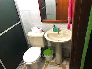 Une petite salle de bain avec des toilettes, un lavabo et une poubelle verte.