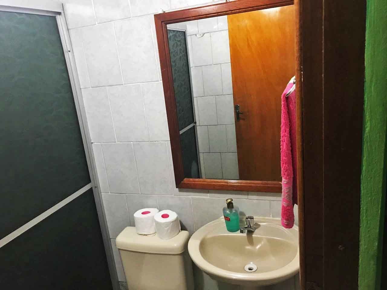 A small bathroom with a toilet, sink, and mirror. There are two rolls of toilet paper on the toilet.