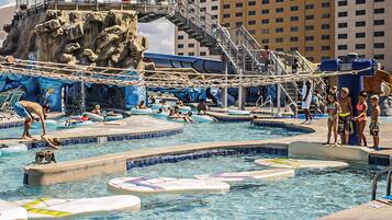 Enjoy water activities at this vibrant water park featuring multiple pools, a rock formation with a water slide, and a rope bridge.