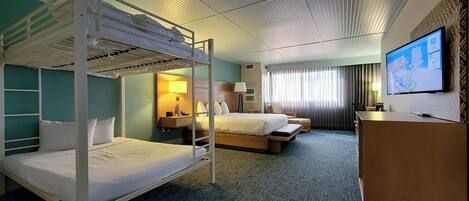 Habitación de hotel con literas, una cama individual, un escritorio, un televisor y una ventana con cortinas.