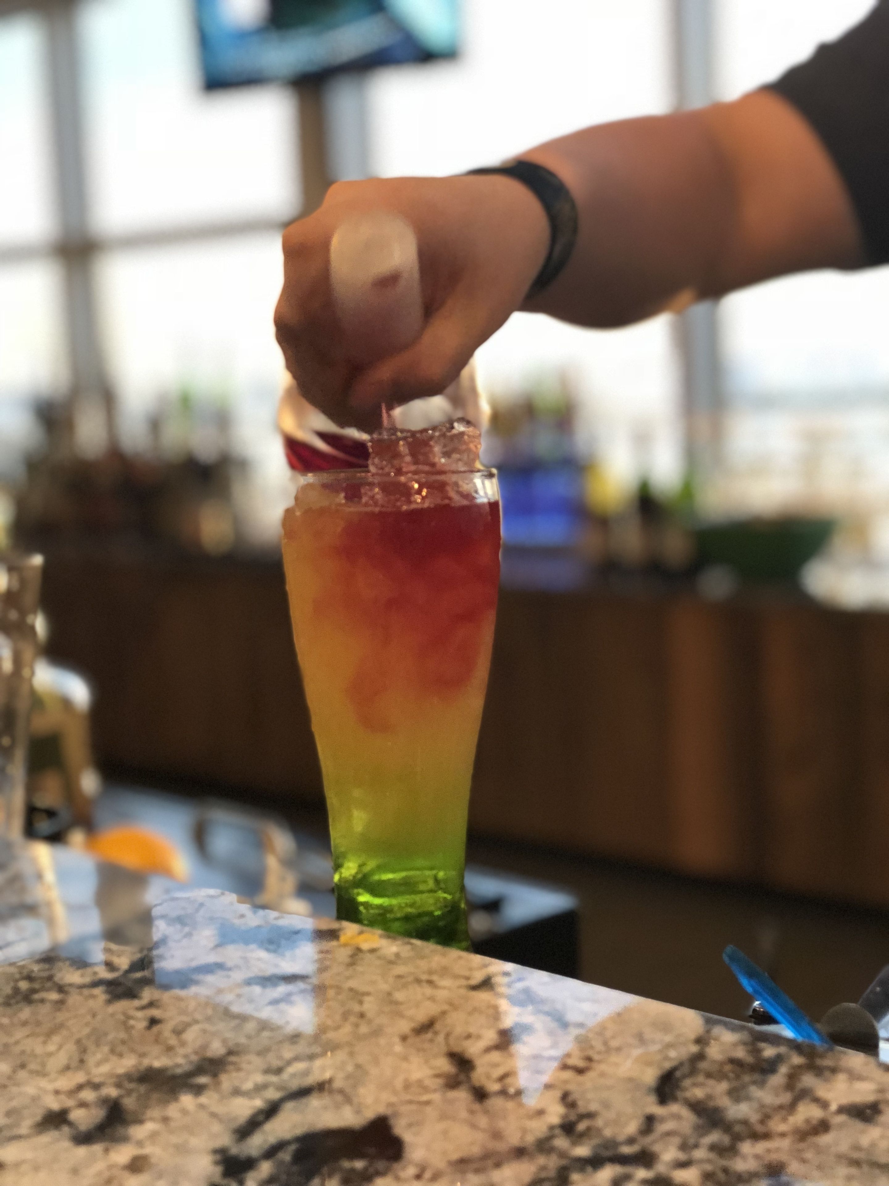 A bar setting with a person preparing a drink in a tall glass.