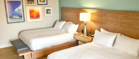 A hotel room with two beds, a nightstand with a lamp, and framed pictures on the wall.
