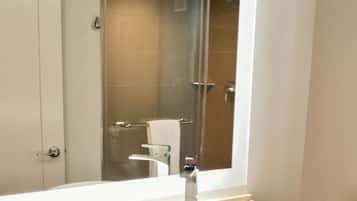 A bathroom with a large mirror, a white sink, and a shower visible in the background.