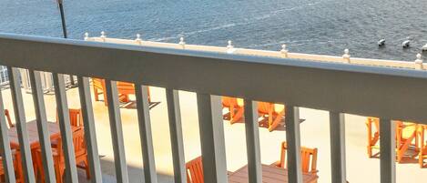 A balcony with orange chairs and tables overlooking a body of water.
