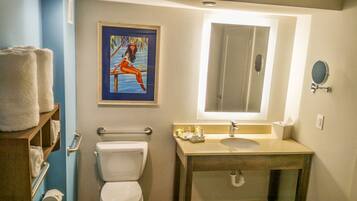 Un baño con inodoro, lavamanos, espejo y un cuadro enmarcado en la pared.