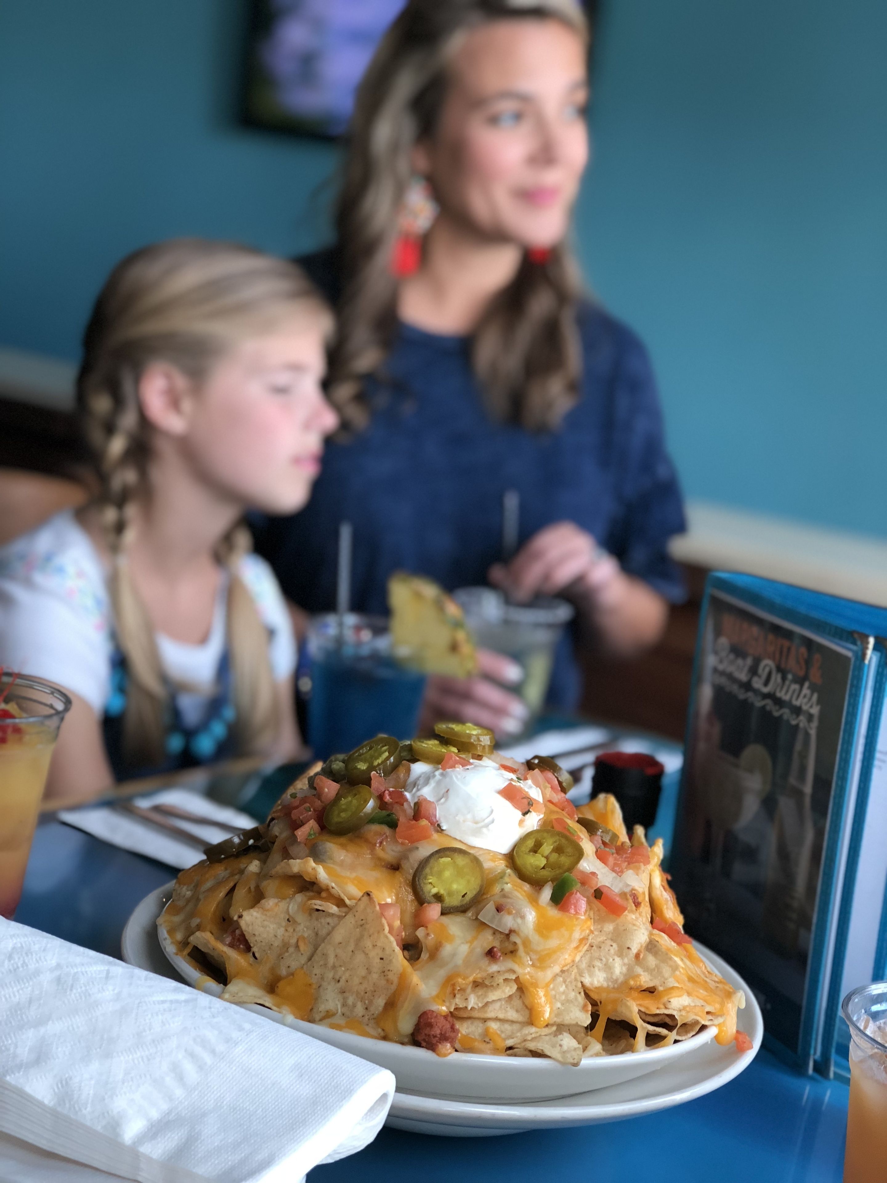 A plate of nachos with toppings, a drink, and a menu on a table.