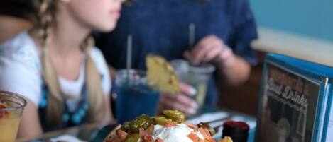 A plate of nachos with toppings, a drink, and a menu on a table.