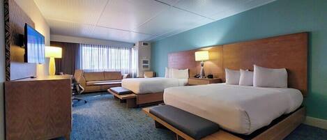 A hotel room with two beds, a desk, a chair, a TV, and a window with curtains.