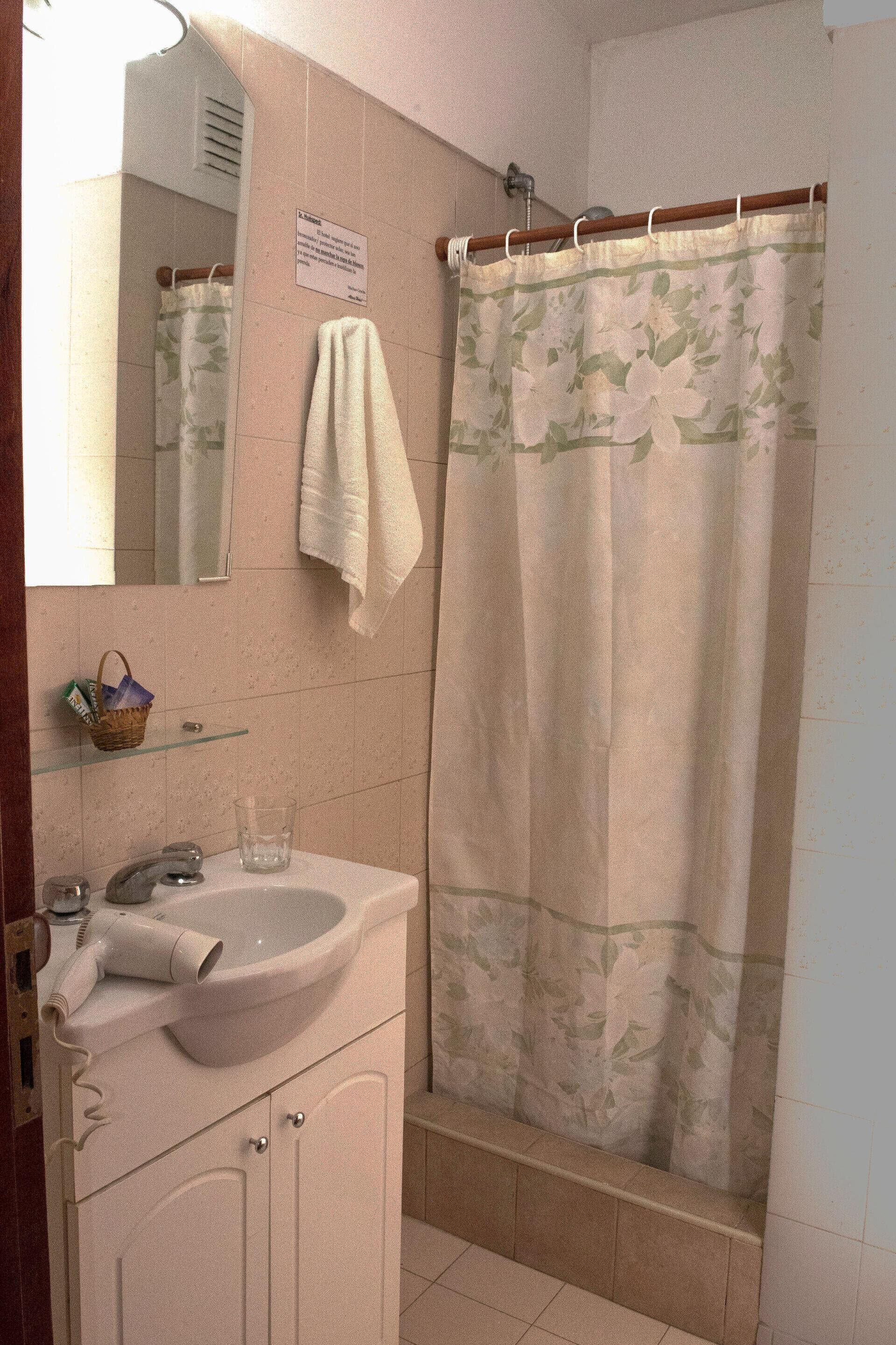 Une salle de bain équipée d’un lavabo, d’un miroir, d’un porte-serviettes, d’un rideau de douche et d’une petite étagère avec un panier.