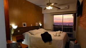 A hotel room with a bed, a desk with a phone, a suitcase, and a window with a view. - Hotel Altair (San Clemente)