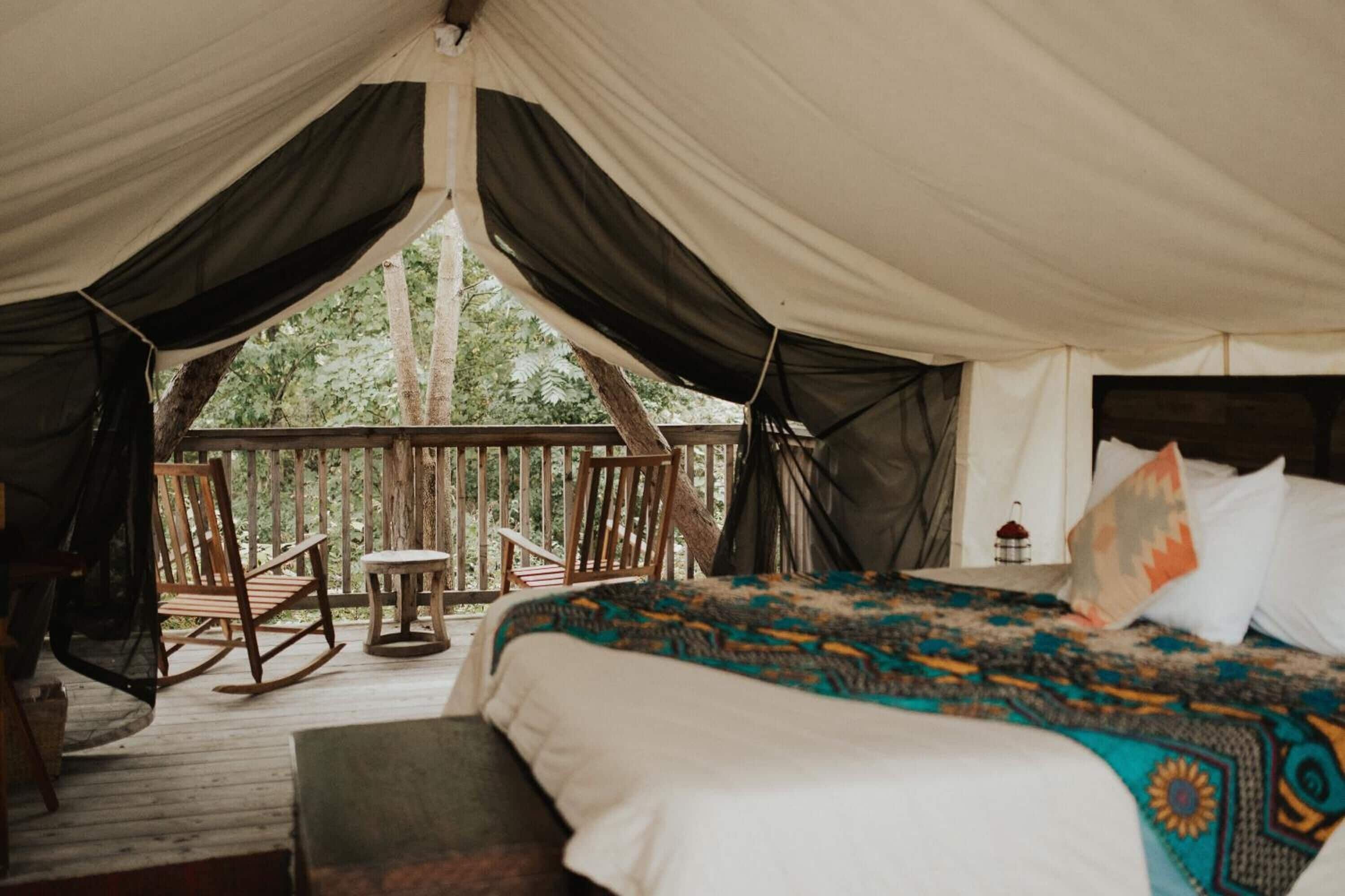 A tented accommodation with a bed, a rocking chair, and a small table.