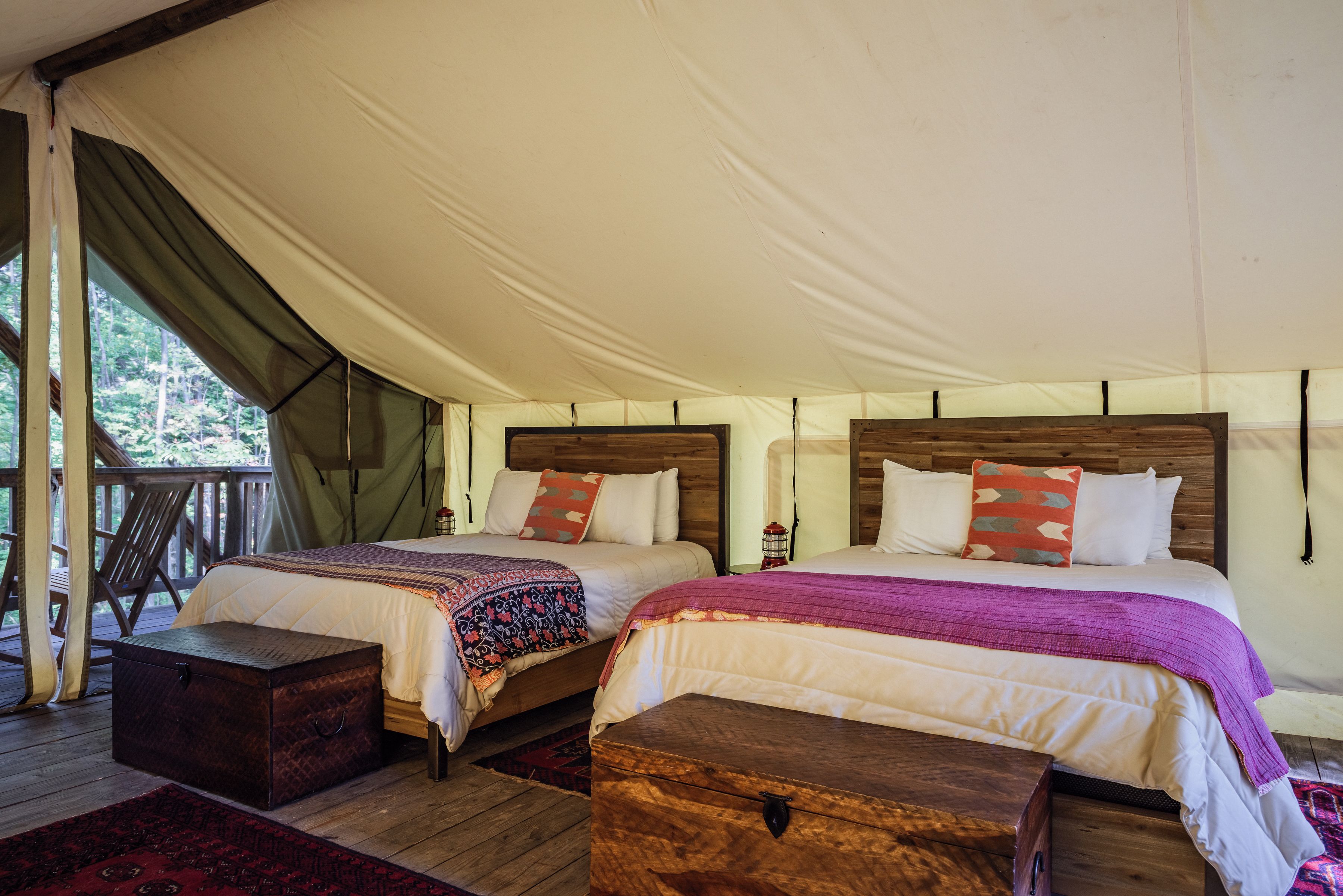 Two beds with wooden headboards in a tent-style room, each with a pillow and a blanket.