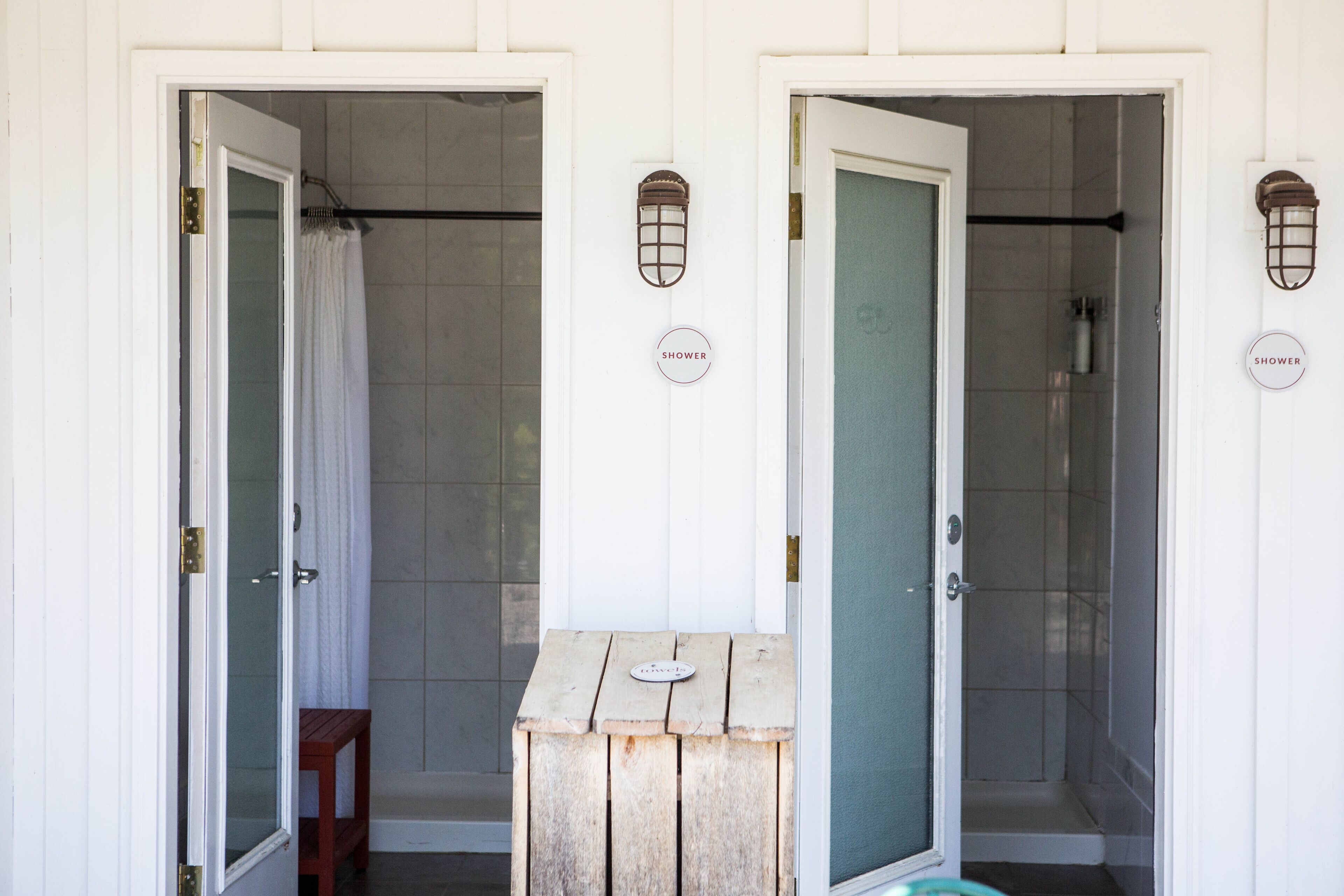 Two shower doors with a wooden bench and a metal lantern between them.