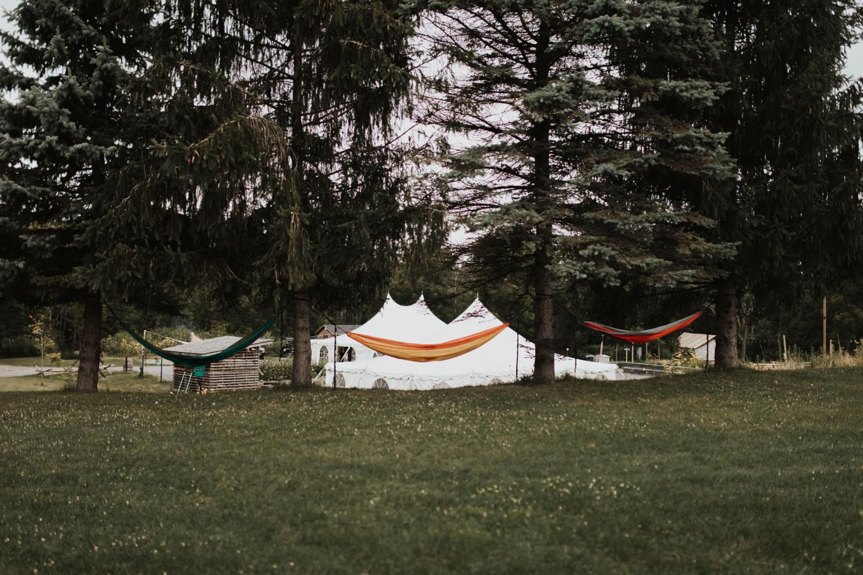 Una carpa blanca con tela roja y naranja, rodeada de árboles en un área cubierta de hierba.