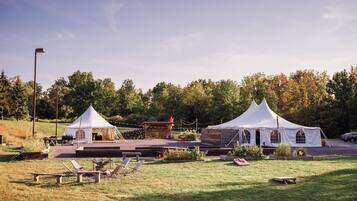 Two white tents with attached structures, a grassy area with lounge chairs, and a paved walkway.