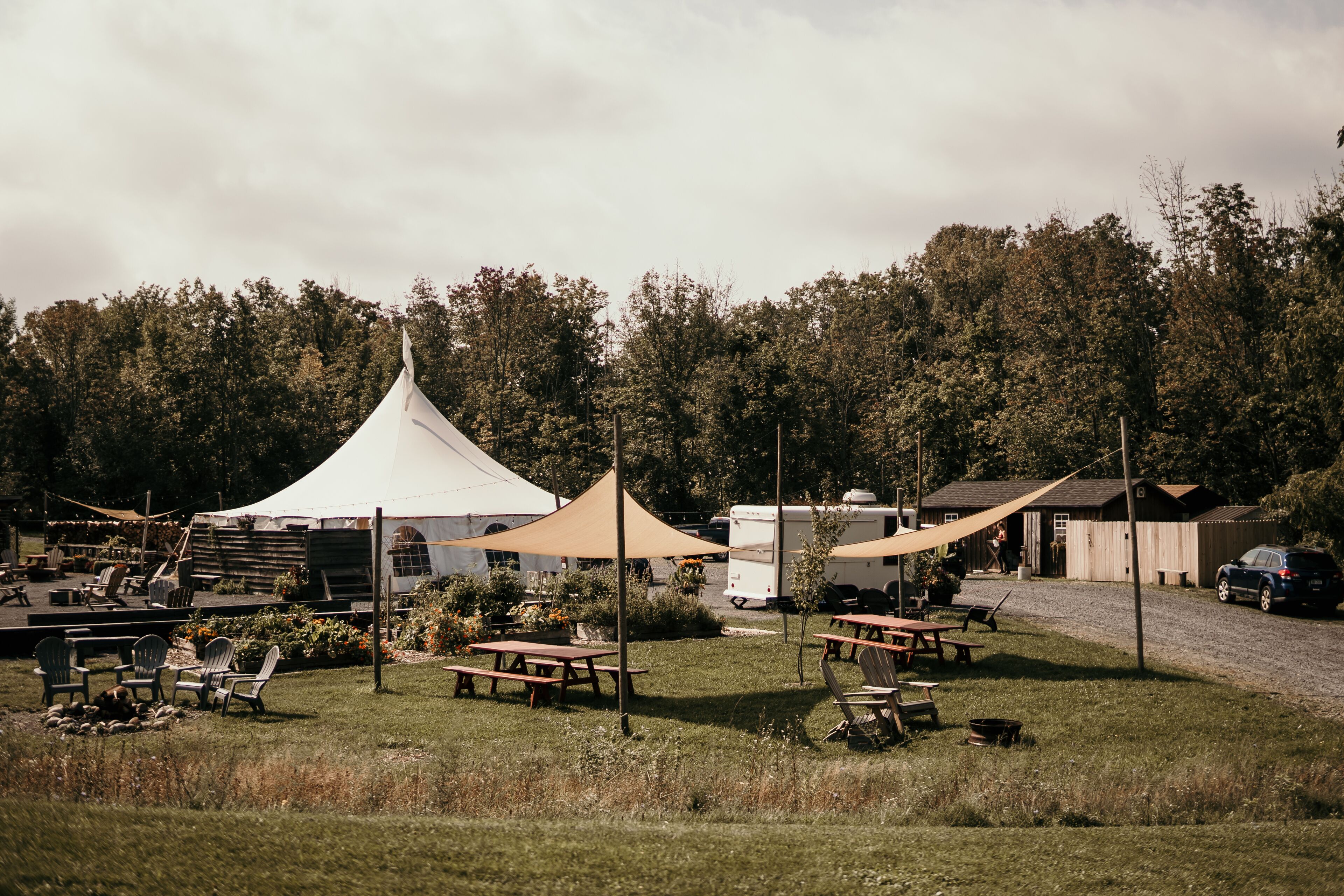 Un camping con mesas de picnic, sillas, una tienda de campaña blanca y vehículos recreativos.