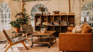 Een gezellige binnenruimte met een houten tafel, een bank en een boekenplank vol boeken en decoratieve objecten.