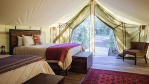 Een tentaccommodatie met twee bedden, een houten bank en een stoel.