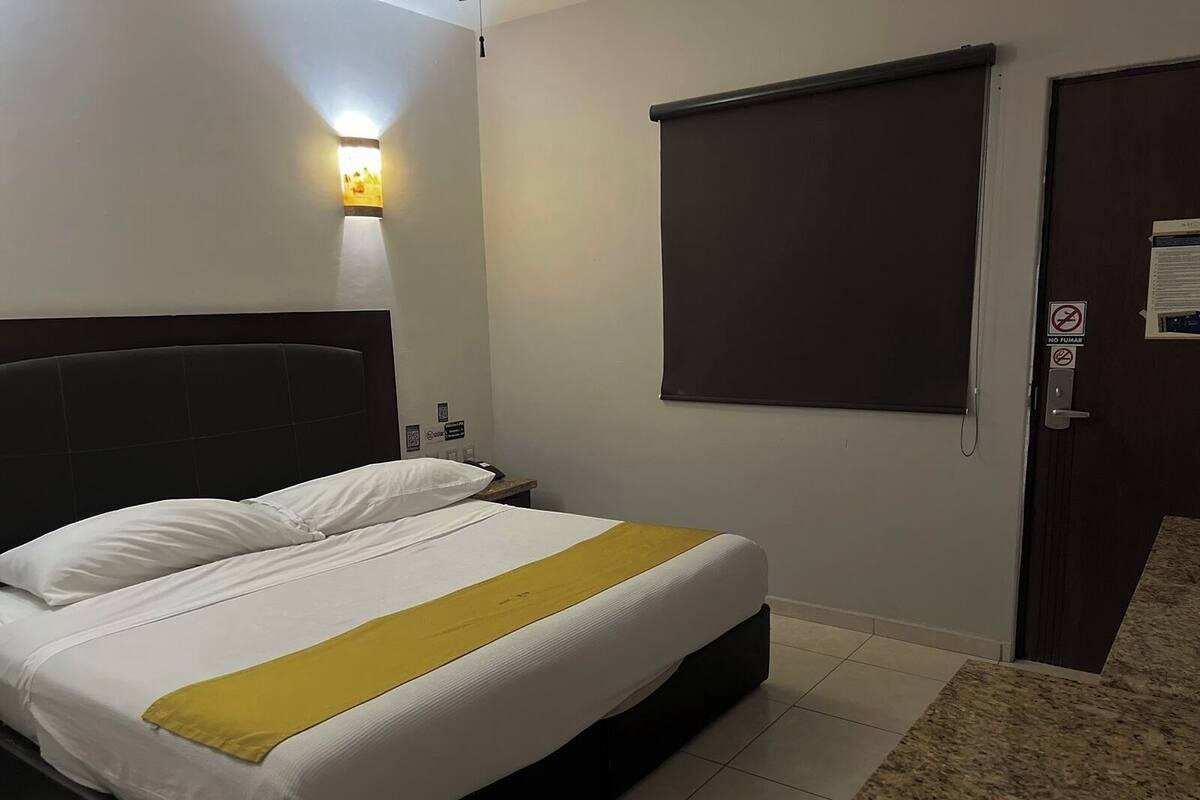 Habitació d'hotel amb un llit, una tauleta de nit, un televisor fixat a la paret i una porta amb un cartell de 'No Fumar'.