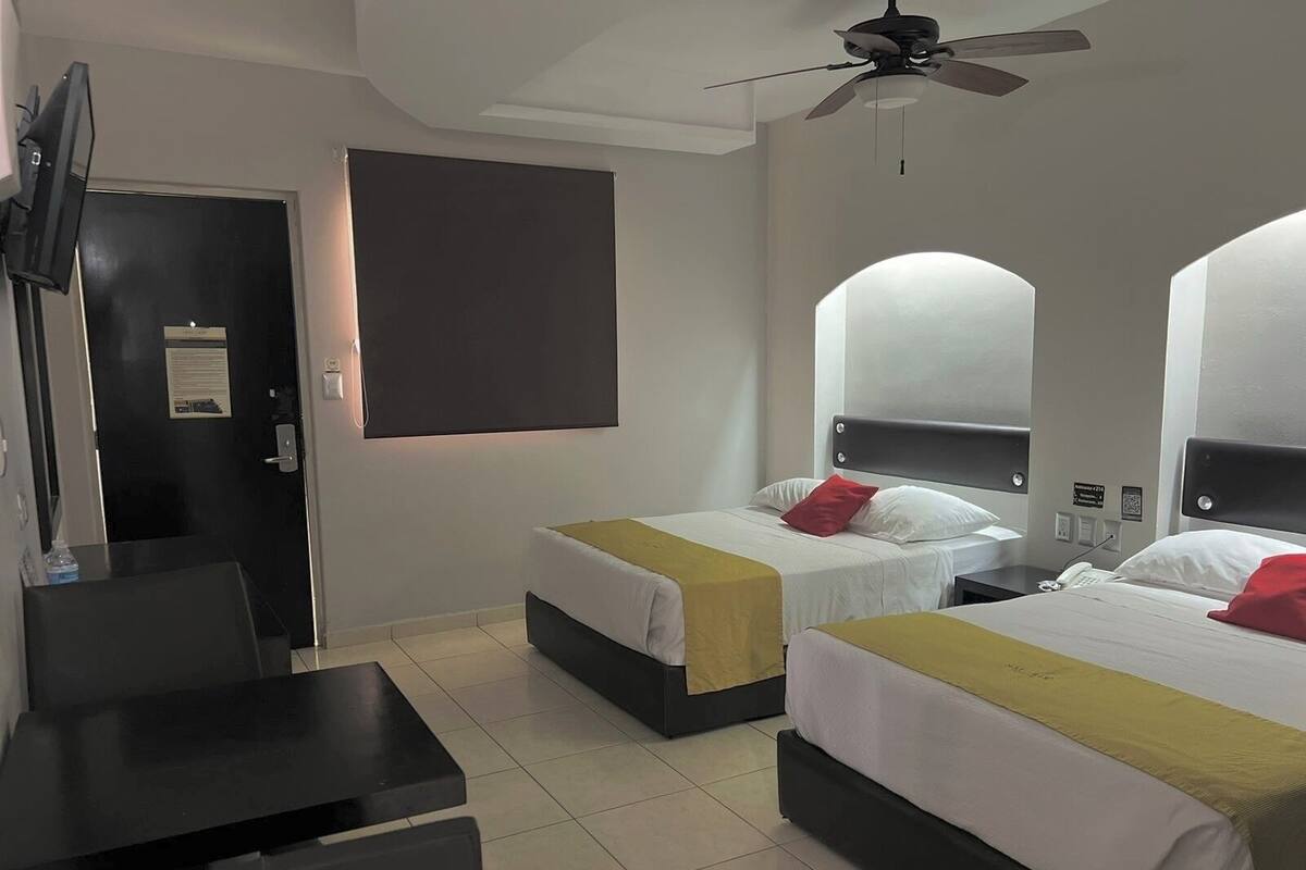 Habitació d'hotel amb dos llits, escriptori, televisió i ventilador de sostre.