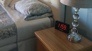 A neatly made bed with a tufted headboard, a bedside lamp, and a digital clock displaying the time.