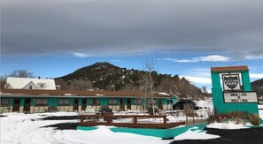 A motel with a sign reading 'Raton Pass Motor Inn' and a question 'Should I stay or should I snow?'