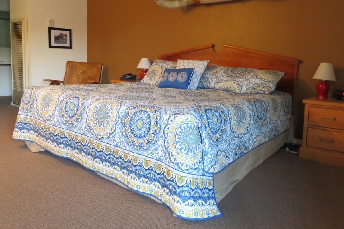 A bed with a patterned bedspread, a wooden headboard, and a wall-mounted horn decoration.