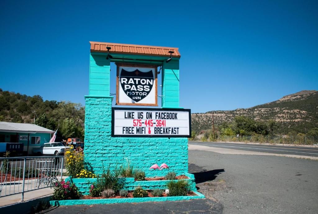A turquoise building with a sign for Raton Pass Motor Inn, including a Facebook link and a phone number.